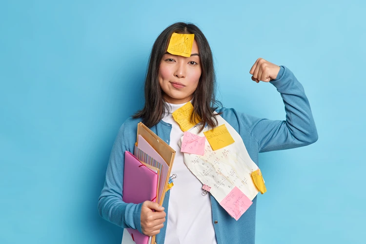 female student raises arm feels confident after working diploma paper wears stickers forehead holds folders