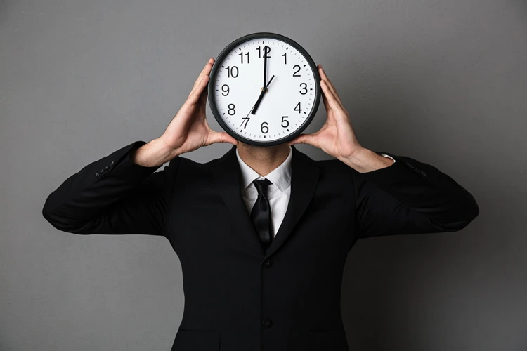 young man black suit holding clock front his face